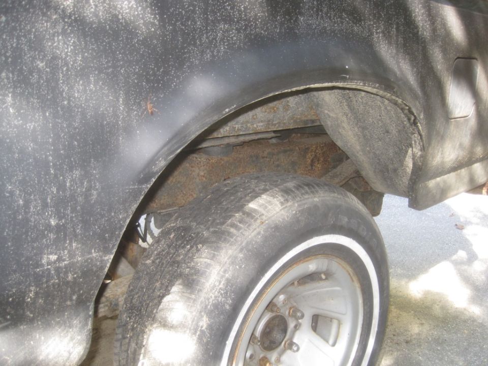 Black vehicle's rusty rear wheel well and tire with whitewall trim