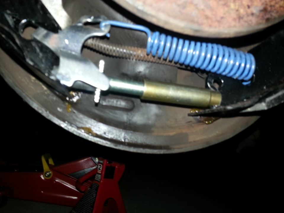 Drum brake assembly with blue spring and metal adjuster, red jack stand visible below