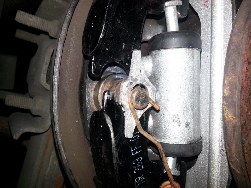 Close-up of a vehicle's rear drum brake assembly, showing the brake shoe, wheel cylinder, and spring mechanism