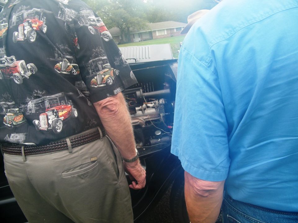 Two men looking at the engine of an old car