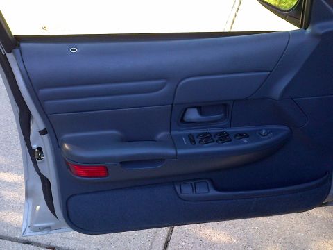 2001 Ford Crown Victoria - Close-up of a car's interior door panel with power window controls and a red reflector.