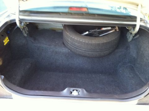 2001 Ford Crown Victoria - The trunk of a car contains a spare tire and jack. The interior is carpeted.