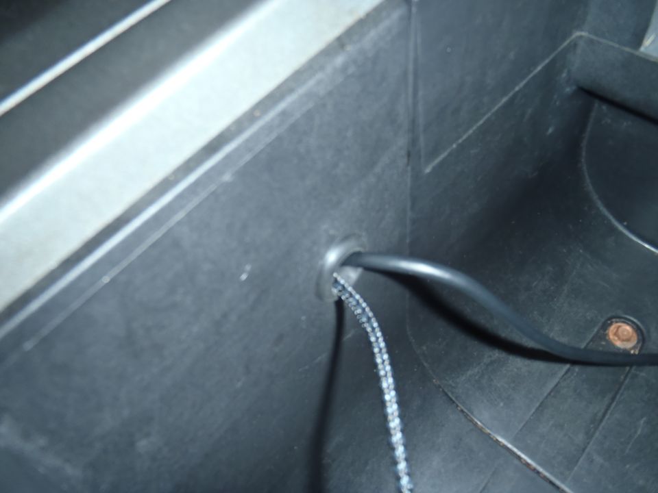 Close-up of a black wire and braided cable passing through a hole in black plastic interior trim