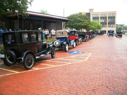 1909 Ford Model T - A line of vintage Ford Model T cars are parked on a brick-paved street in front of a building.