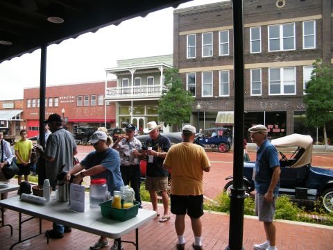 1909 Ford Model T - A gathering of people with several antique cars on display in a town square.