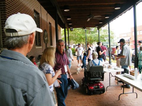 1909 Ford Model T - A group of people are socializing on a covered patio, with a mobility scooter parked nearby.