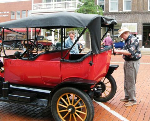 1909 Ford Model T - A red 1909 Ford Model T touring car is parked on a brick street, with two men attending to it.