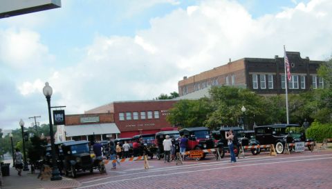 1909 Ford Model T - A collection of antique cars are displayed on a cobblestone street, with spectators observing the vehicles.