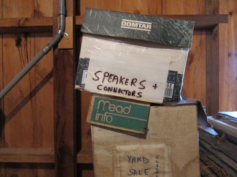 1991 Ford LTD Crown Victoria - Boxes are stacked in front of a wooden wall, with labels indicating contents and a yard sale.