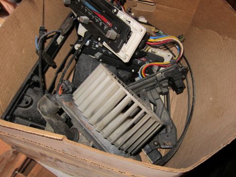 1991 Ford LTD Crown Victoria - Assorted car heater control panels and blower motor parts piled in a cardboard box.