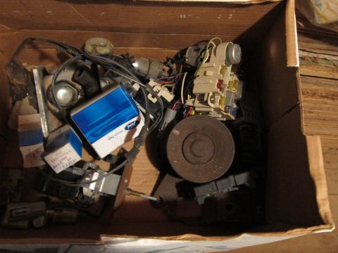 1991 Ford LTD Crown Victoria - A collection of automotive parts, including electrical components and packaged items, are stored within a cardboard box.
