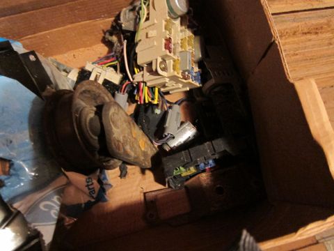 1991 Ford LTD Crown Victoria - A collection of automotive electrical parts, including fuse boxes and wiring, are stored in a cardboard box.