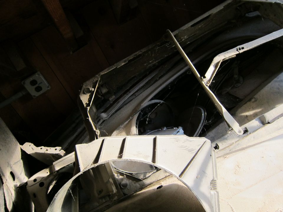 Disassembled car parts, including hood hinges and fender sections, stored indoors