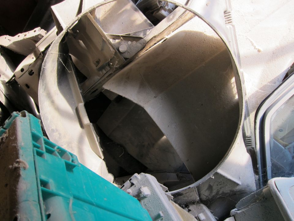 Pile of broken car parts, including a large, dusty, circular metal piece and a green plastic bin
