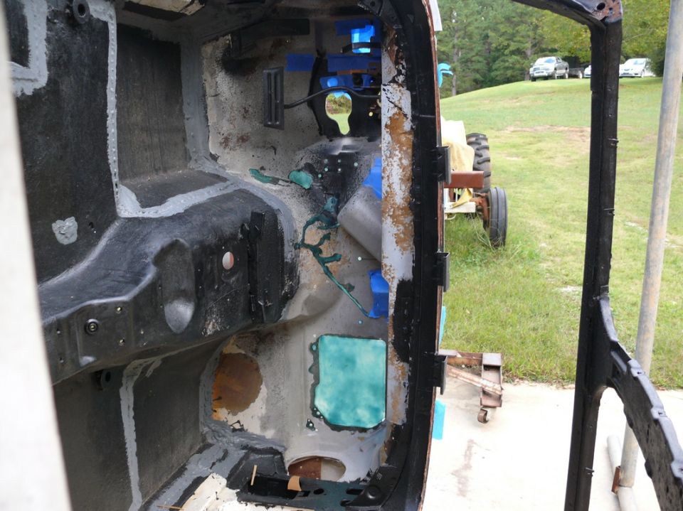 Car interior showing firewall and floor pan during restoration, with a tractor and cars visible in the background