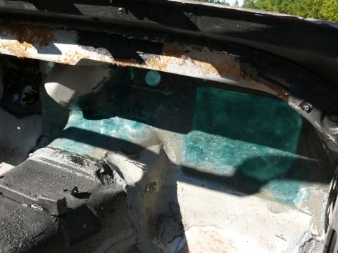 Car interior showing rust and green fiberglass repair on the passenger side floor pan