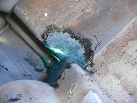 Close-up of underbody rust repair with blue sealant and black tar