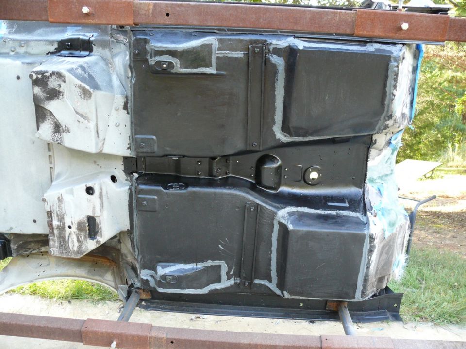 Car frame underside with black undercoating and grey sealant applied to various panels