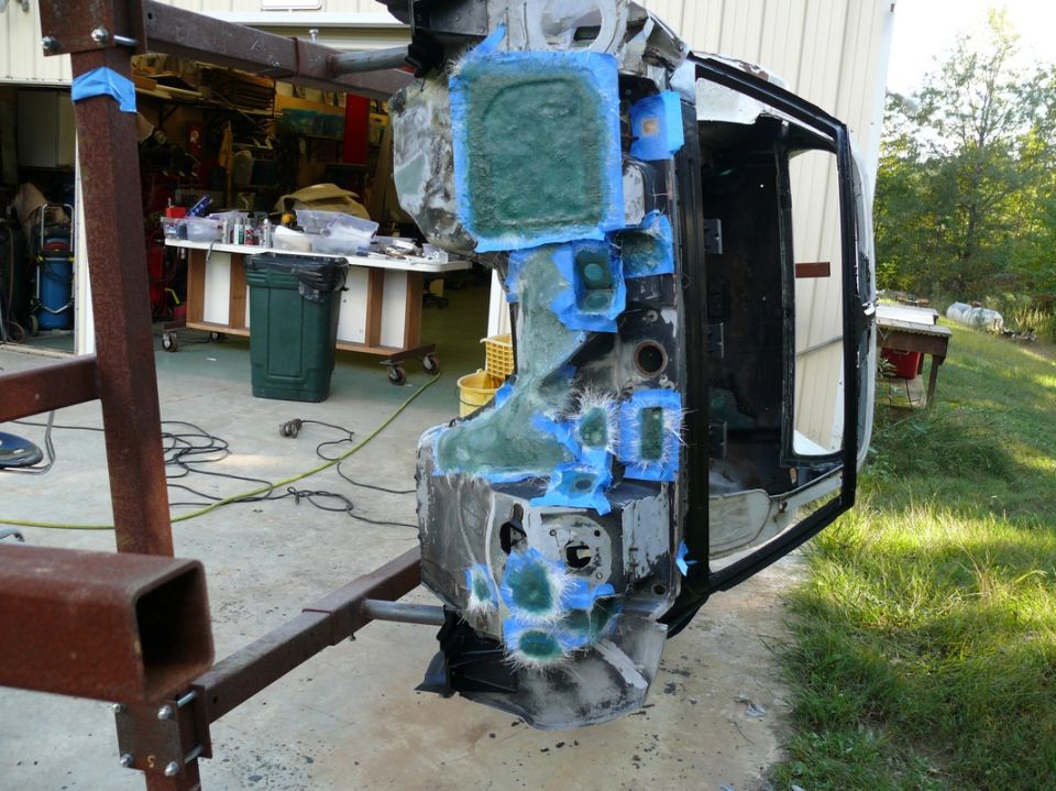 Car body section with fiberglass and blue tape repairs, suspended on a frame