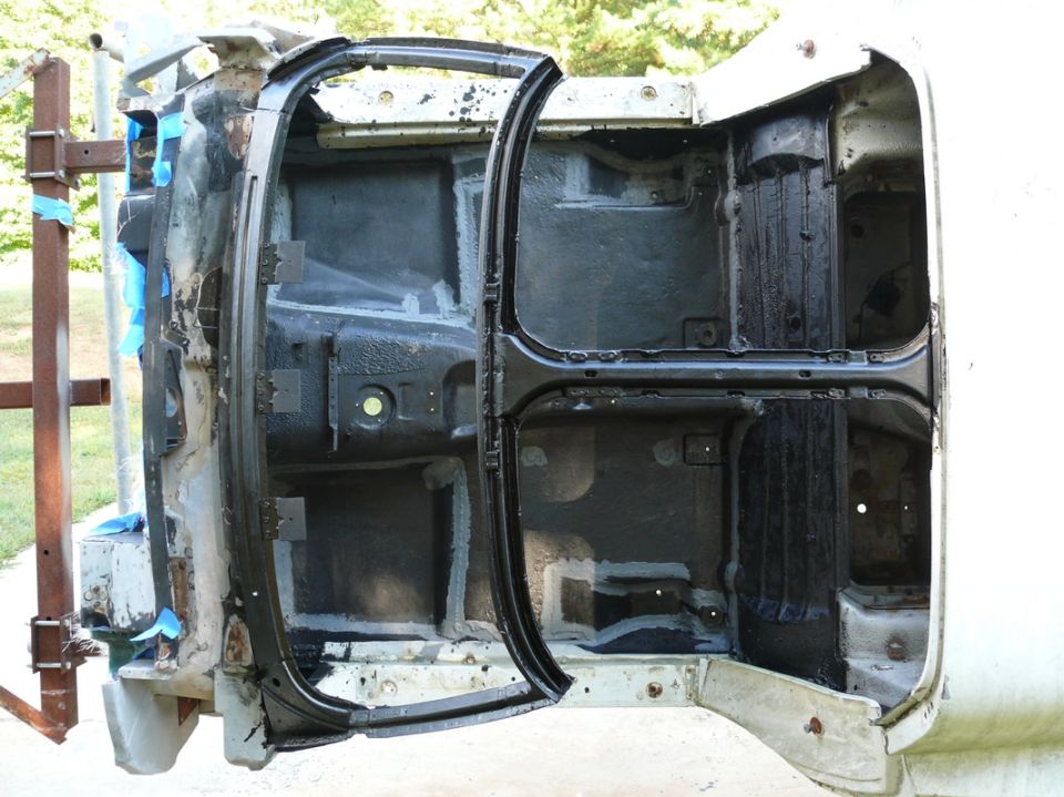 Car body frame with doors open, showing interior structure. Supported by a metal frame