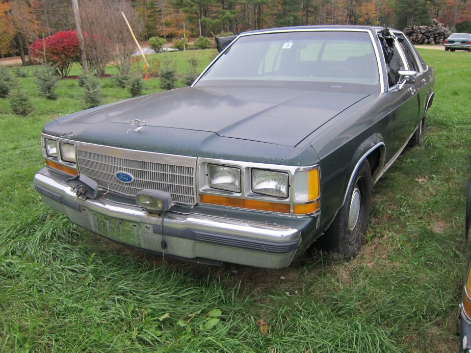 Front view of a dark green 1990s Ford Crown Victoria parked on grass. Chrome grille and bumper are visible