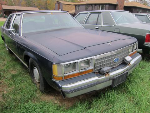 1991 Ford LTD Crown Victoria - A dark blue Ford Crown Victoria sits in a grassy area next to another vehicle.
