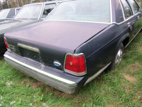 1991 Ford LTD Crown Victoria - Rear view of a dark blue sedan parked in grass, with another vehicle beside it.