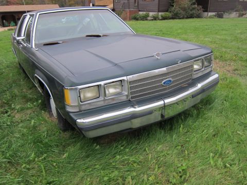 1991 Ford LTD Crown Victoria - A dark green sedan sits on a grassy lawn, showing its front grille and headlights.