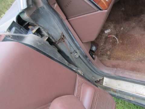 1991 Ford LTD Crown Victoria - Close-up of a car's interior door frame, showing signs of rust and wear, exposed wiring on the floor.