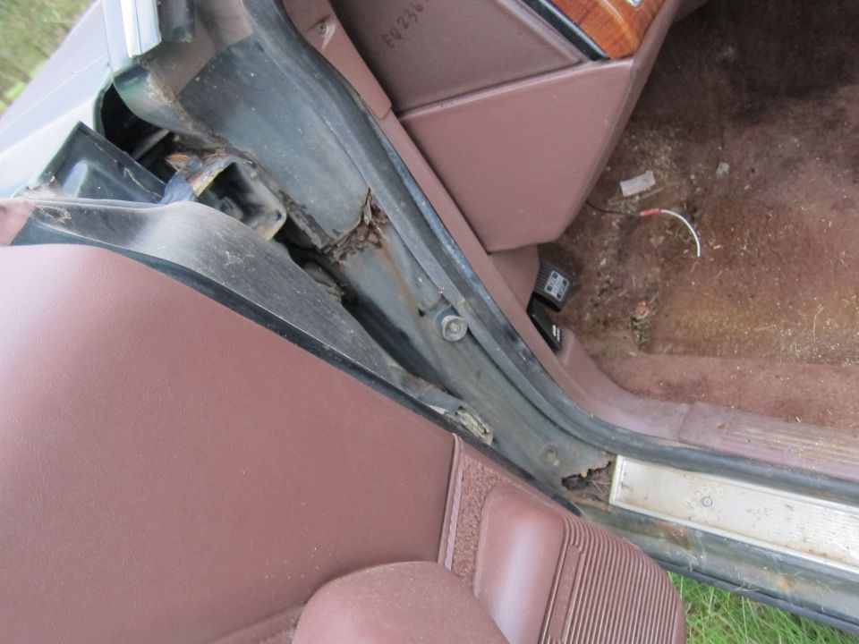 Car interior door frame with visible rust and brown upholstery. Some wiring is exposed on the floor