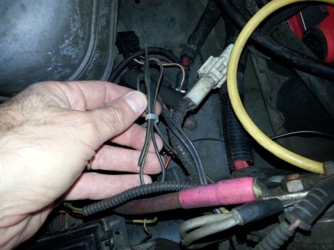 1992 Ford Bronco - Close-up view of a hand manipulating electrical wires within a vehicle's engine compartment.