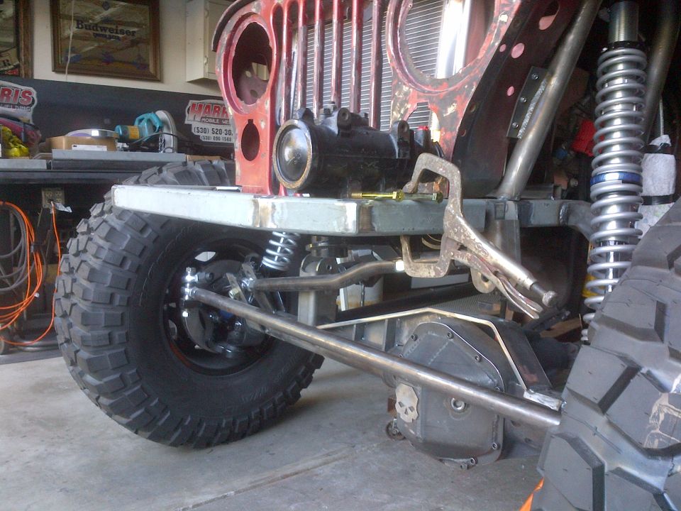 Red Jeep CJ-series front end with large off-road tires, custom suspension, and a clamp on the frame