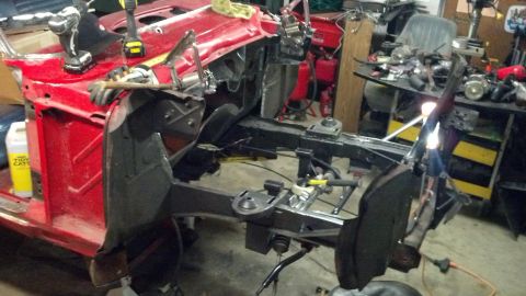 1964 Ford Fairlane - A car's chassis and front body panels are disassembled in a workshop, with tools and equipment visible in the background.