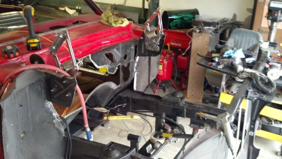 Car body undergoing restoration in a workshop, showing disassembled front end and chassis components