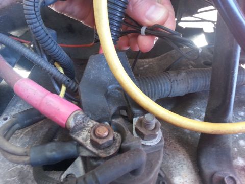 1992 Ford Bronco - A close-up view of a vehicle's wiring harness and starter solenoid, with a hand holding wires.