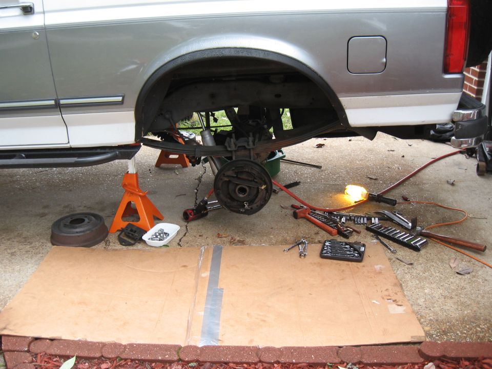 Truck rear axle assembly on jack stands, brake drum removed, tools scattered on cardboard