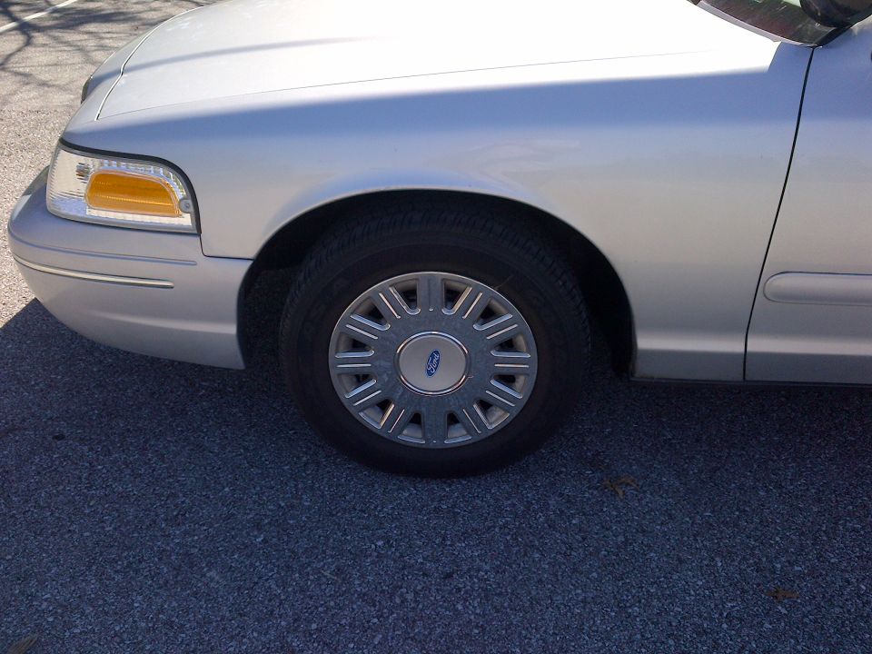 Silver 2001 Ford Crown Victoria front fender, headlight, and wheel with a Ford logo