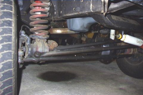 1979 Ford F-150 - Close-up of the undercarriage, focusing on the steering and suspension system with a visible oil stain on the ground.