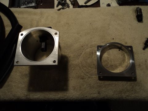 2004 Mercury Grand Marquis - Two aluminum throttle body adapter pieces are laid out on a textured cloth surface, with various hardware scattered in the background.