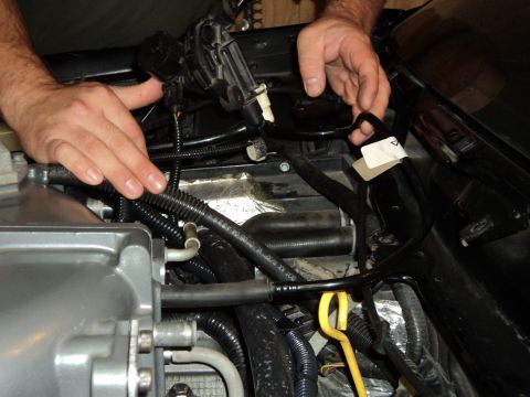2004 Mercury Grand Marquis - Hands work on the engine bay wiring harness, with a yellow dipstick visible.
