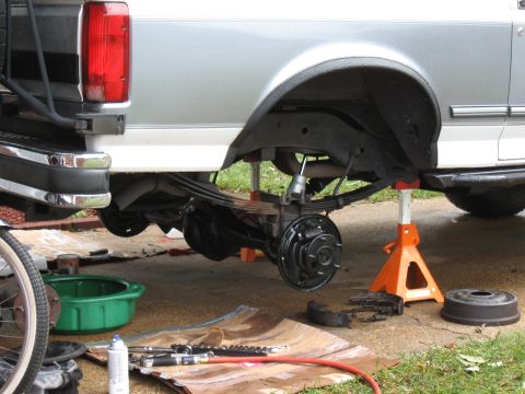 1994 Ford Bronco - The rear axle and suspension of a silver 1992 Ford F-150 truck are visible, supported by jack stands during brake maintenance.