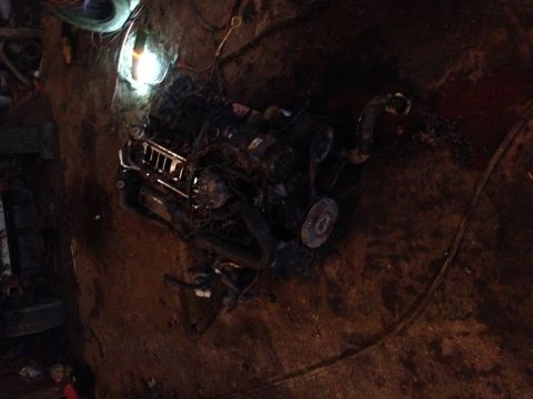 1995 Ford F-150 - Engine assembly in a dirt pit, with visible wiring and a light source overhead.