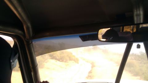 1996 Ford Bronco - View from inside a vehicle with a roll cage, looking out at a dusty off-road landscape.