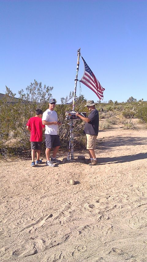 1996 Ford Bronco - People gather around a flagpole in a dry, sandy area with sparse vegetation under a clear blue sky.