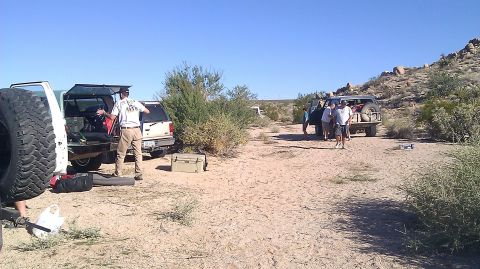 1996 Ford Bronco - Multiple SUVs are parked in a desert landscape, with people milling about near one of the vehicles.