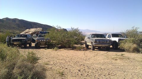 1996 Ford Bronco - Several SUVs, including a 1996 Ford Bronco, are parked in a desert area with sparse vegetation.