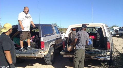 1996 Ford Bronco - Two Ford Broncos are parked side-by-side with their tailgates down as people load supplies.