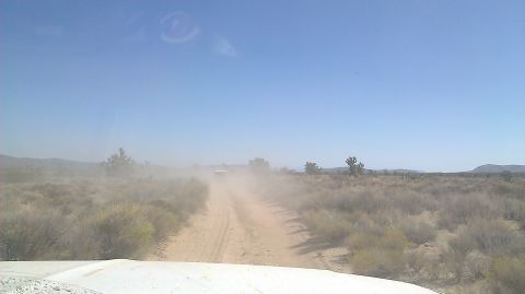1996 Ford Bronco - A white SUV kicks up dust on a dirt road in a dry, arid landscape under a clear blue sky.