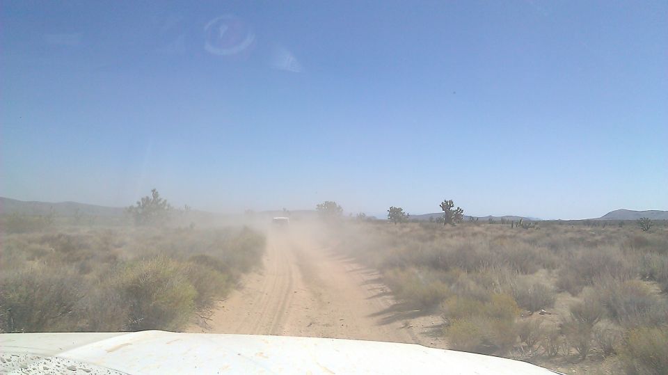 Dust cloud from a white SUV on a dirt road in a desert landscape