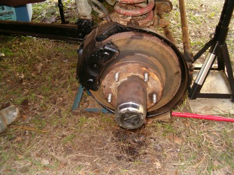 1979 Ford Bronco - Close-up of a vehicle's brake assembly, showing the rotor, caliper, and hub, with a red rod nearby.